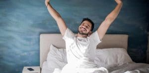 Hombre feliz estirando sus brazos al despertar en su cama